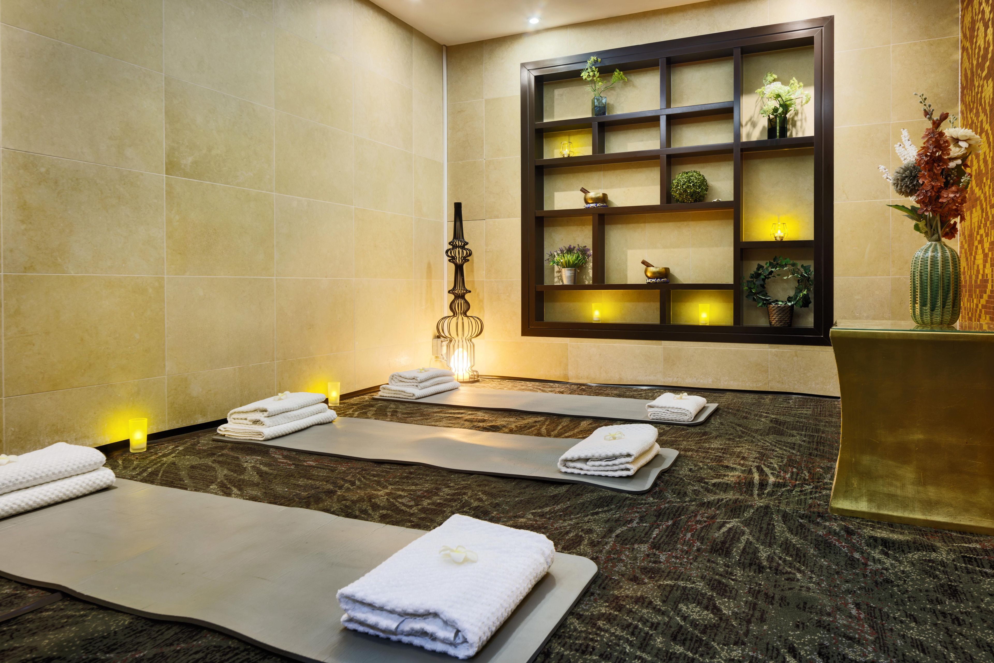 A spa room with massage tables, towels, and a decorative shelf with plants and candles.
