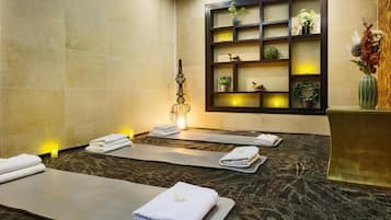 A spa room with massage tables, towels, and a decorative shelf with plants and candles.