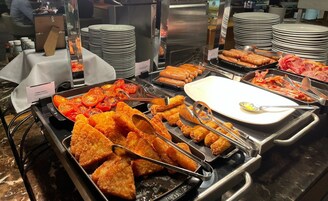Un bufé con diversos alimentos, incluyendo tomates a la parrilla, pollo frito y salchichas.