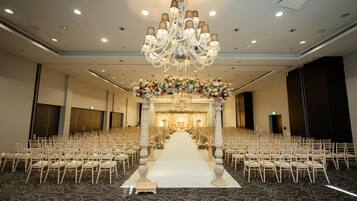A large hall with rows of chairs, a central aisle, and a decorative floral arrangement at the front.