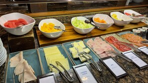 A buffet with various food options including fruits, cheeses, and meats. - Hilton London Syon Park (Brentford)