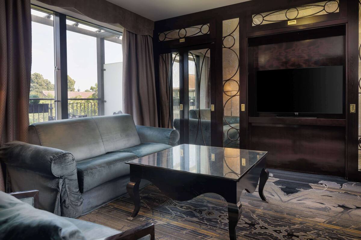 Uma sala de estar moderna com um sofá de couro, uma mesa de centro de vidro e uma TV de tela plana fixada em uma parede escura.