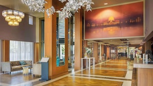 A spacious lobby with a wooden floor, a reception desk, a sofa, and a large wall mural. - Hilton London Syon Park (Brentford)