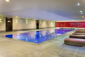 A swimming pool with a tiled floor, a clock, and a wall with a red patterned design. - Hilton London Syon Park (Brentford)