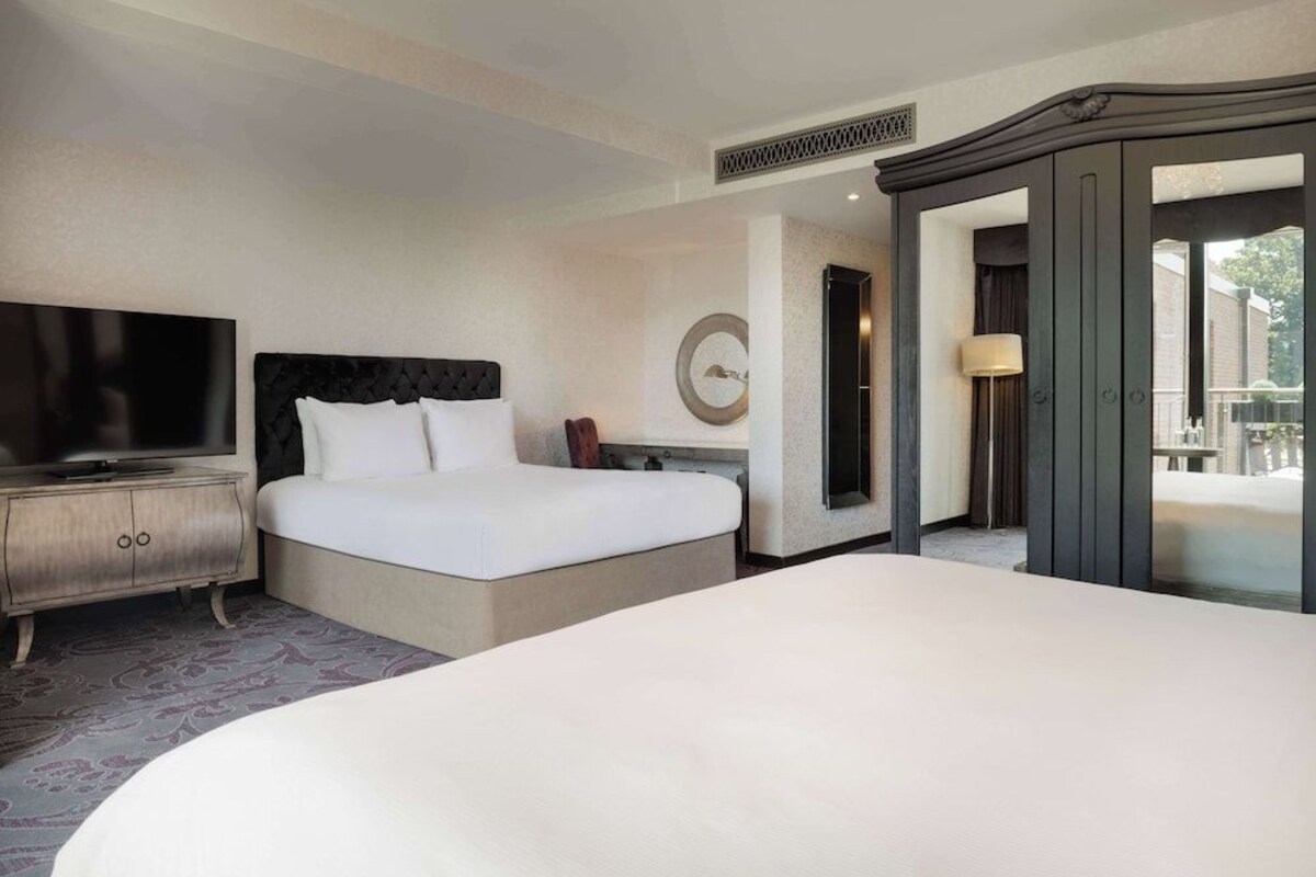 A hotel room with a large bed, a television on a wooden cabinet, a mirror, and a door leading to an outdoor area.