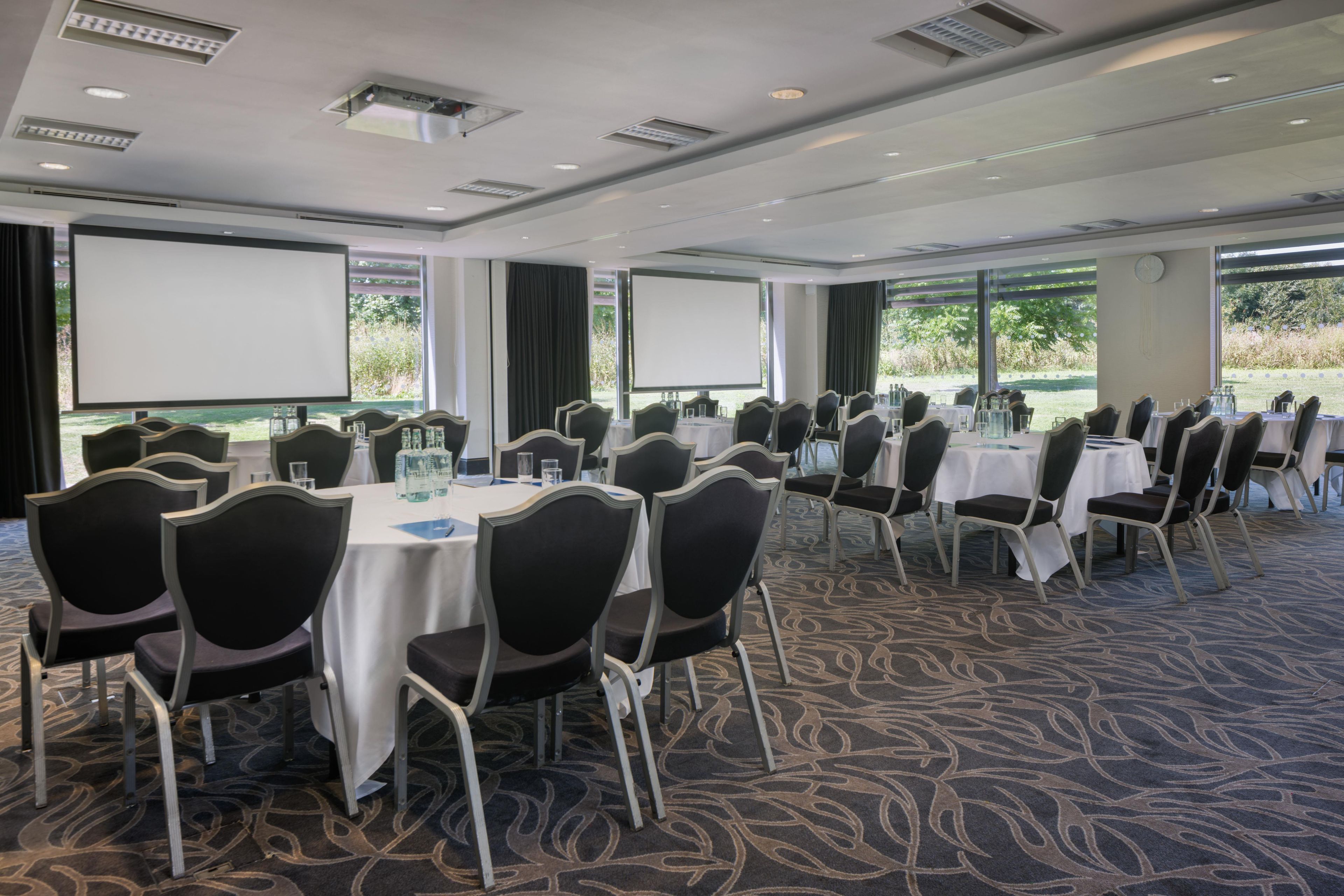 A conference room with tables, chairs, and a projector screen.