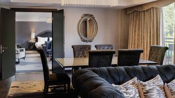 A modern living room with a black leather sofa, a dining table with chairs, a large mirror, and a view of a balcony.