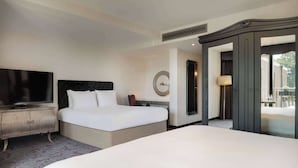 A hotel room with a large bed, a television on a wooden cabinet, a mirror, and a wardrobe. - Hilton London Syon Park (Brentford)