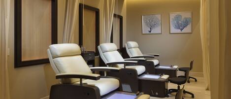 A room with four reclining chairs, each with a footrest and a control panel, suggesting a massage or relaxation area.