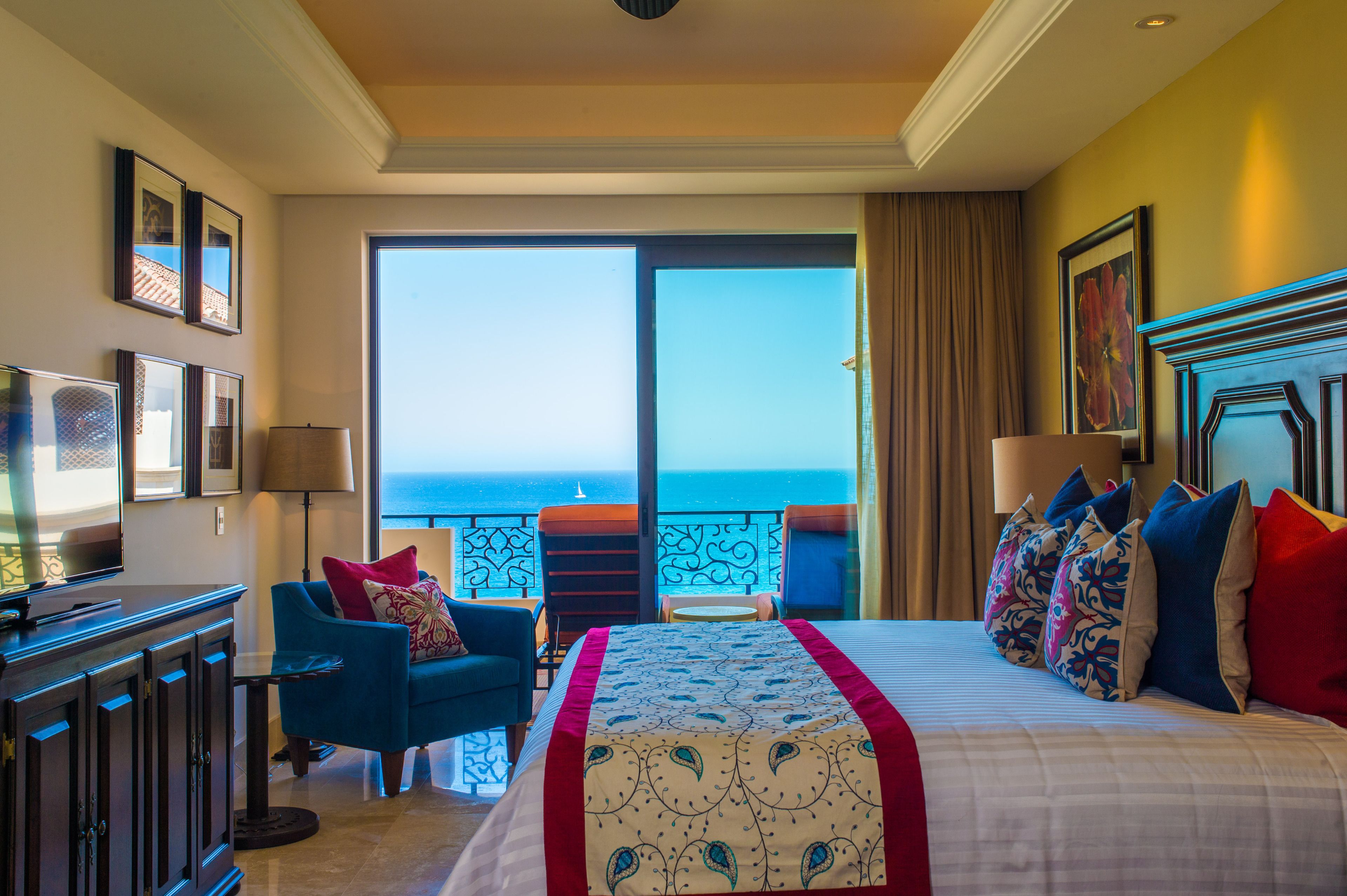 A hotel room with a large bed, a sofa, a TV, and a balcony with a view of the sea.