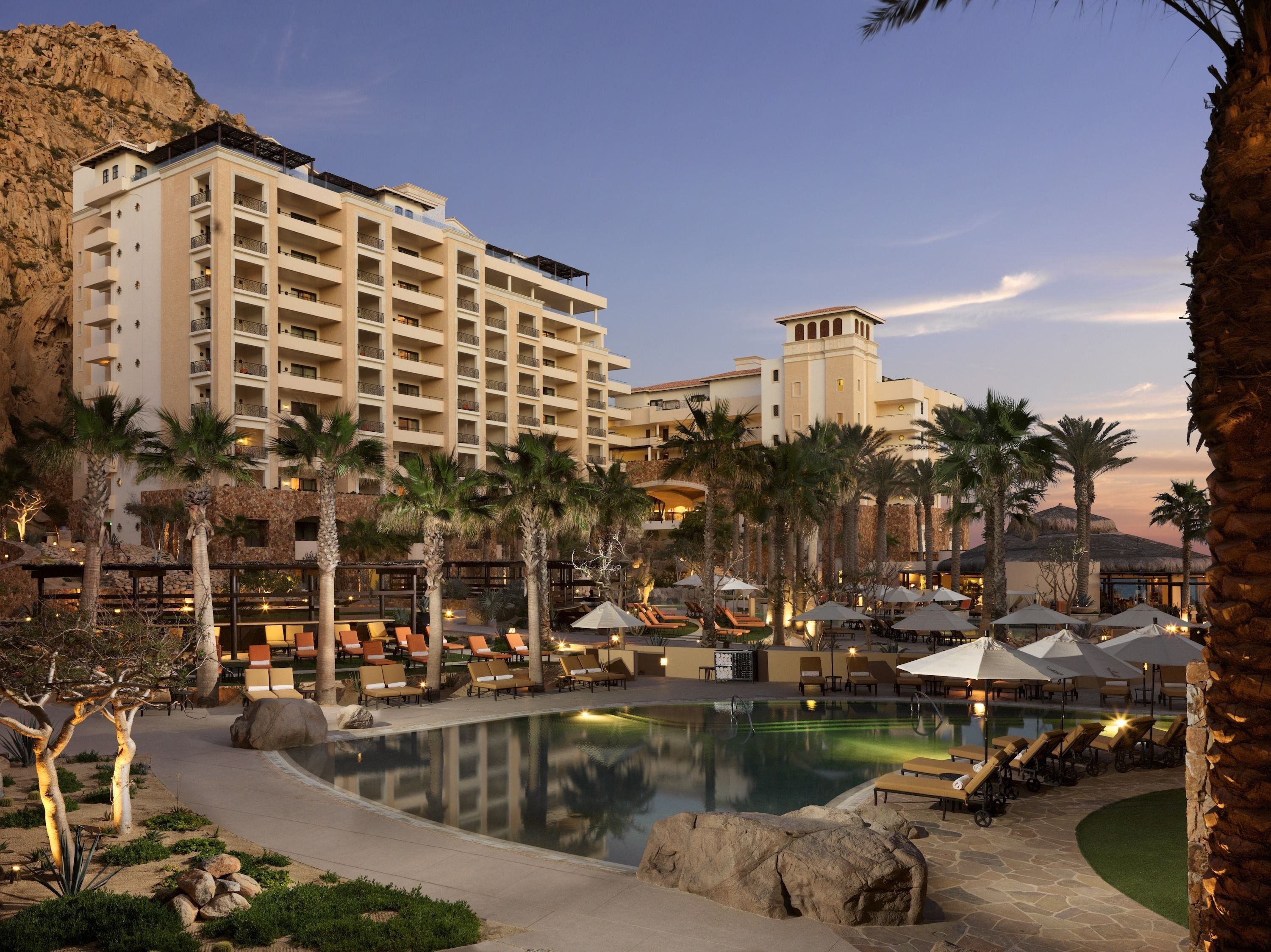 A resort with a large pool, palm trees, and a multi-story building with balconies.
