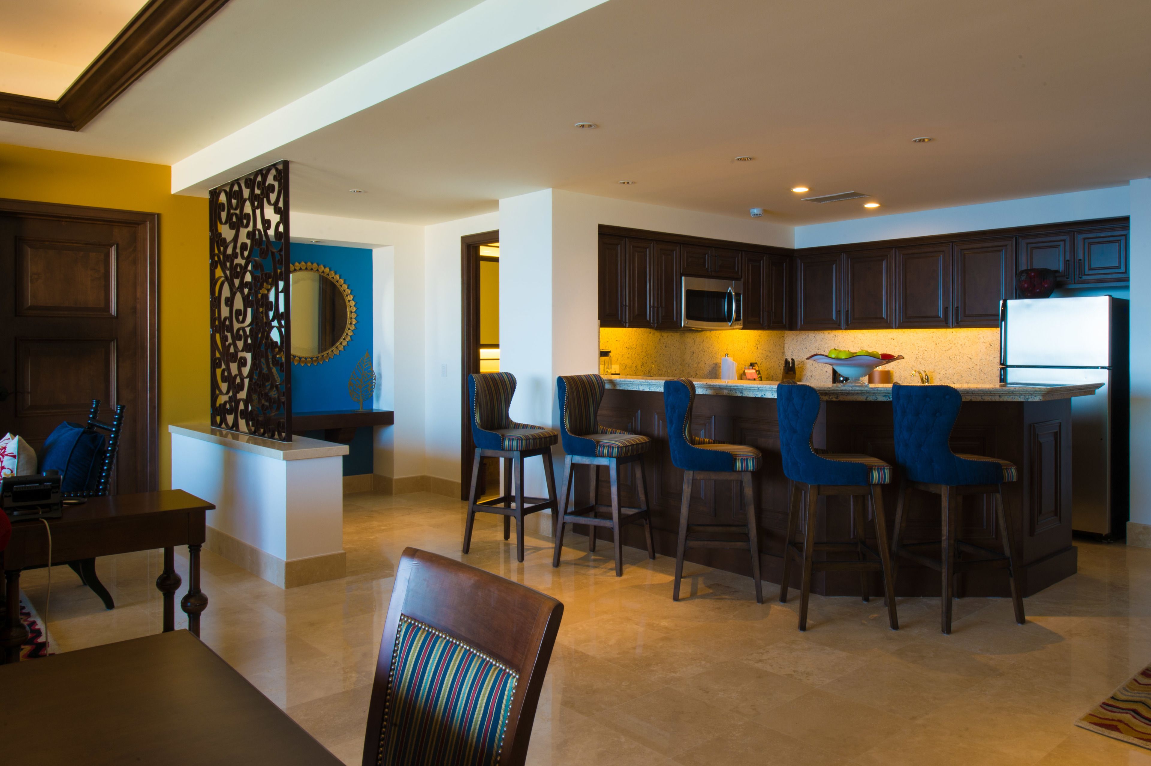 A modern kitchen with dark wooden cabinets, a central island with bar stools, and a microwave above the island.