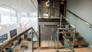 Een modern interieur met een trap, glazen balustrades en een eetgedeelte met tafels en stoelen.