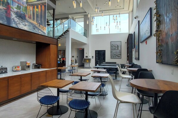 Un café moderne doté de plusieurs espaces de détente, comprenant des tables et des chaises, ainsi qu’un comptoir où est affiché le menu.