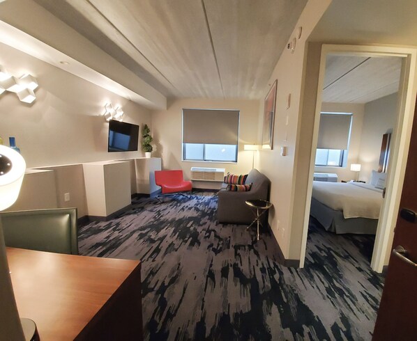 Habitación de hotel con una cama grande, un escritorio, una silla roja y un televisor montado en la pared.