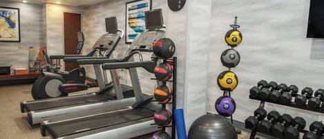 A gym with treadmills, weight machines, and a variety of dumbbells and exercise balls.