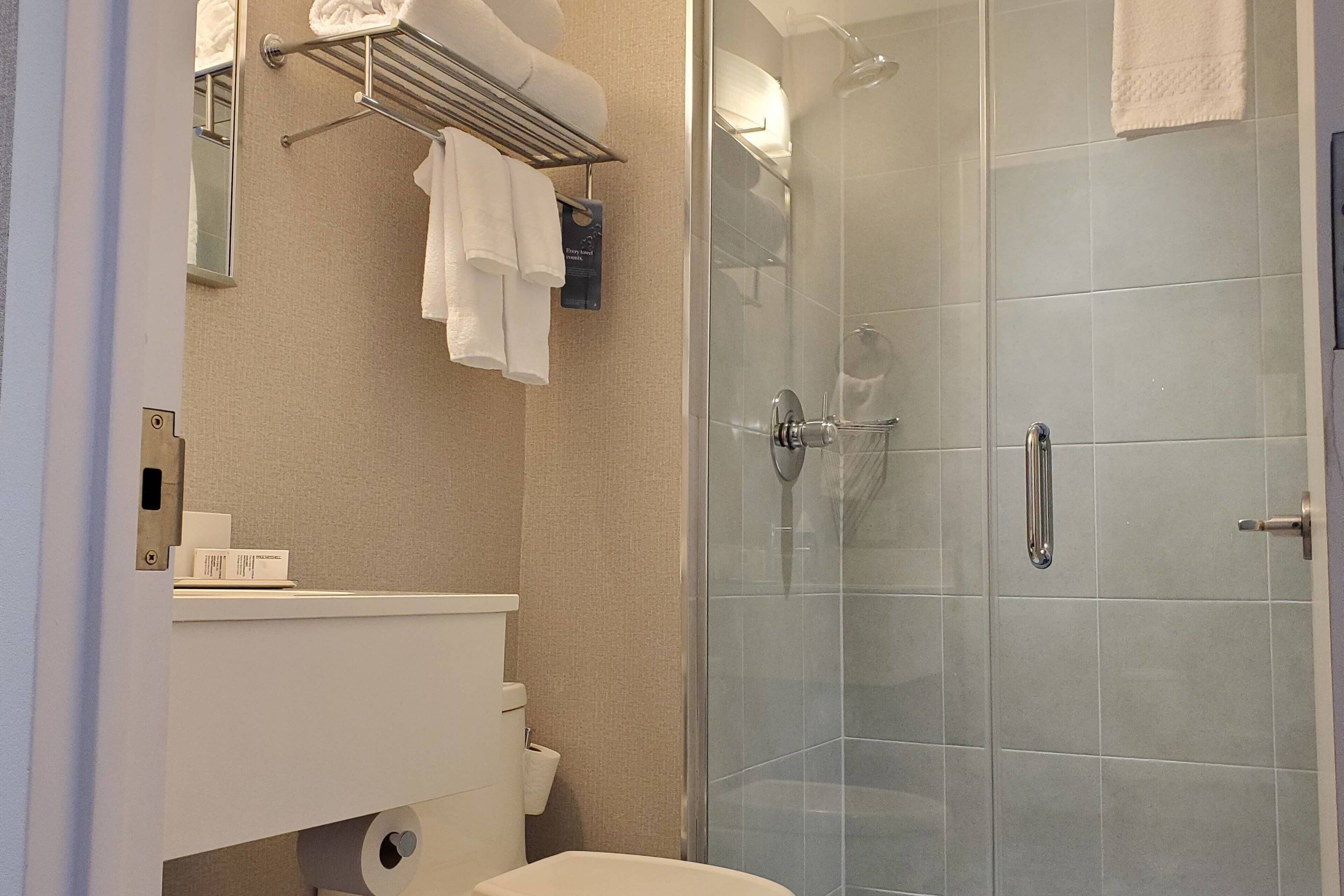 Ein modernes Badezimmer mit einer Duschkabine aus Glas, einem weißen Waschbecken und einem Handtuchhalter mit mehreren Handtüchern.