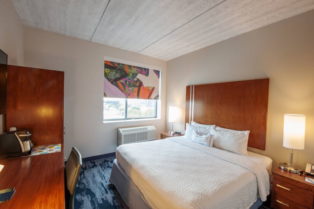 Hotelkamer met een groot bed, een bureau, een stoel, een raam met uitzicht, een radiator en een kunstwerk aan de muur.
