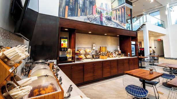 Een modern café met een bedieningsbalie, zitgedeelte en een muurschildering van een stadsstraat.