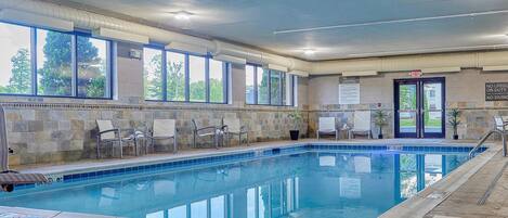 An indoor swimming pool with clear blue water, stone walls, and multiple windows.