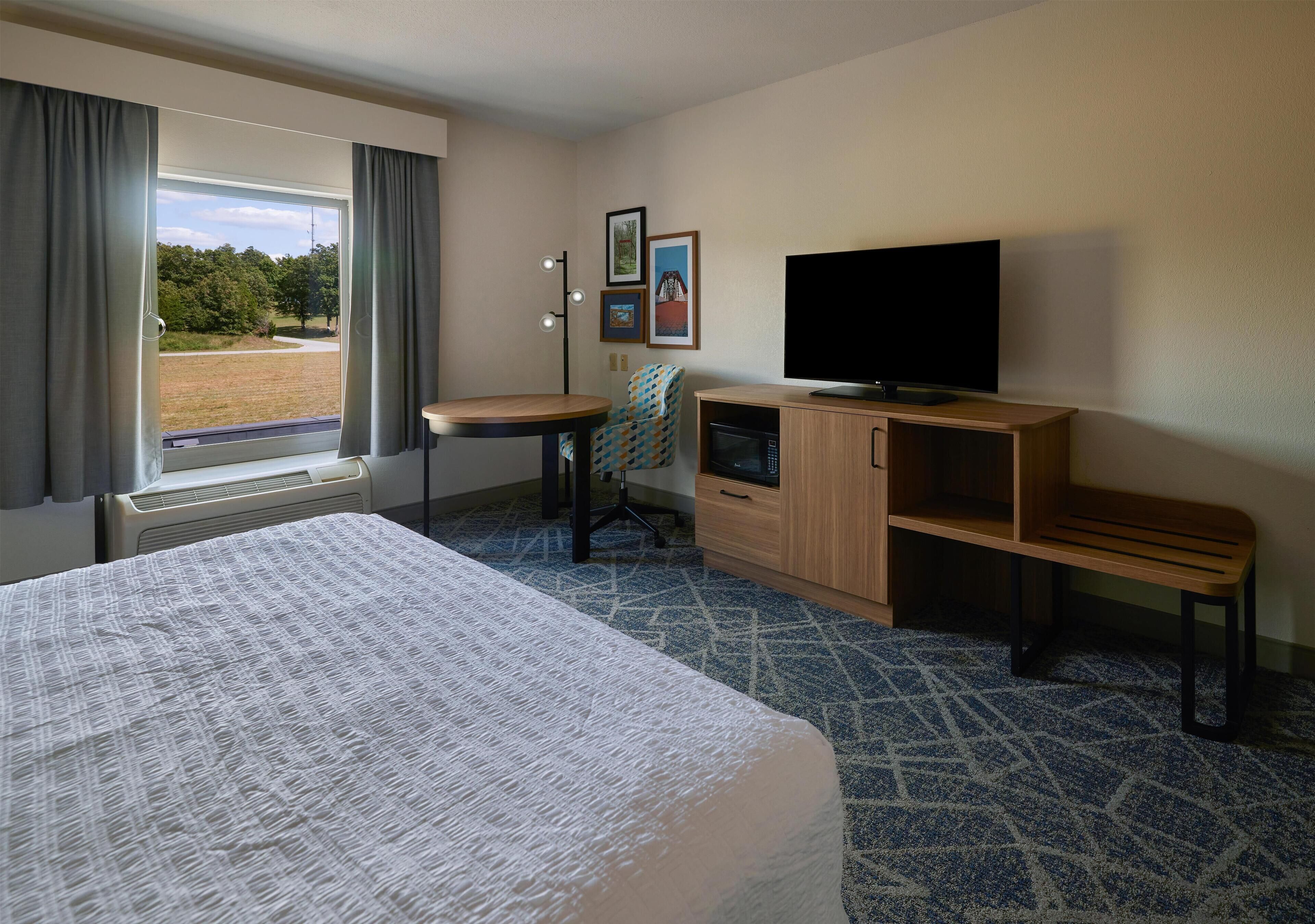 A hotel room with a bed, a desk, a television, and a view of the outdoors.