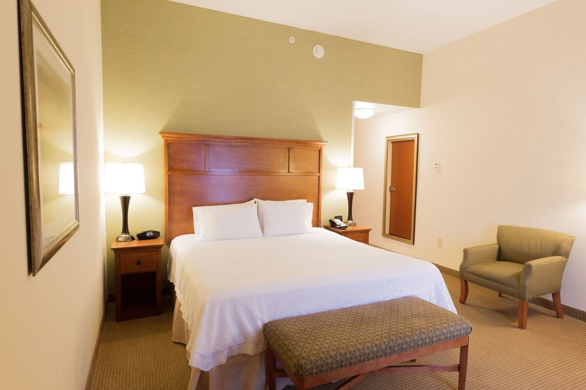 A hotel room with a bed, bedside tables, a chair, a bench, and a door.