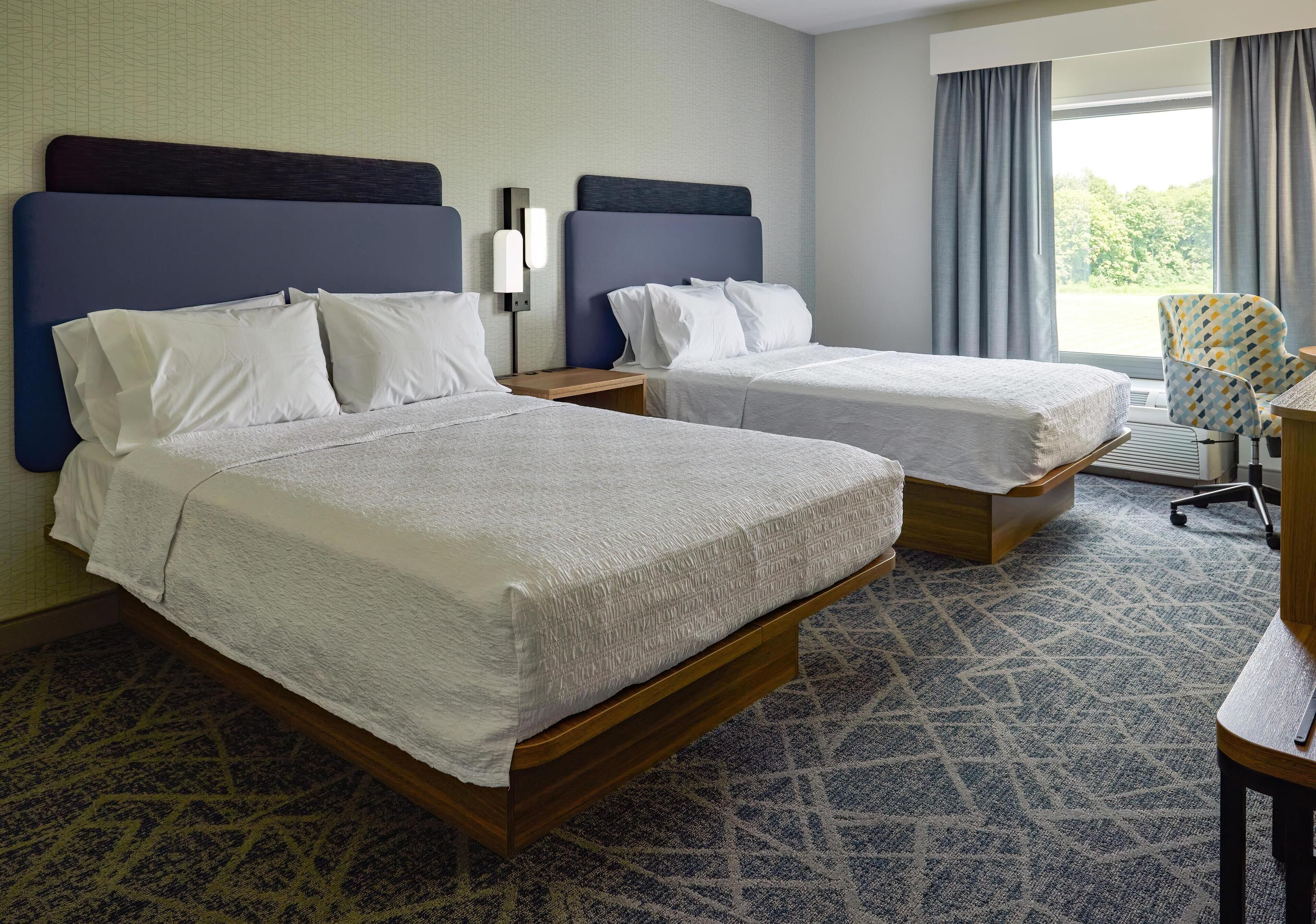 A hotel room with two beds, a desk, and a chair.