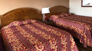 Ein Hotelzimmer mit zwei Betten, jeweils mit einem gemusterten Überwurf, einer Nachttischlampe und einem Nachttisch.