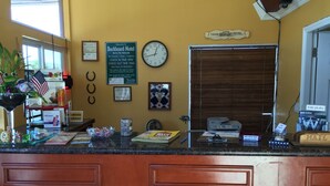 Ein Hotelrezeptionstresen mit einer Uhr, einem Willkommensschild und verschiedenen Annehmlichkeiten wie Drucker, Postfach und Dekoration.