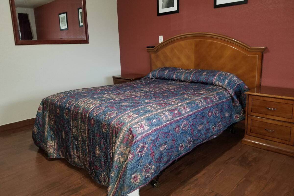 A bedroom with a wooden bed, a nightstand, a dresser, and a mirror on the wall.