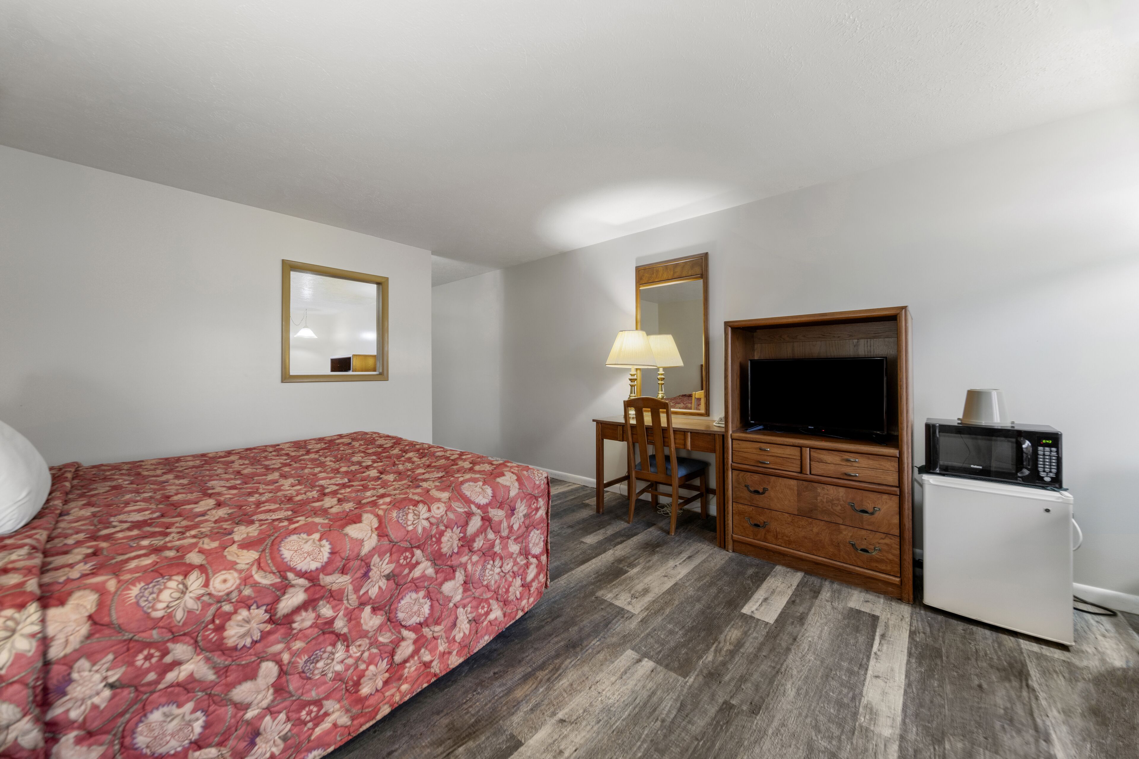 Una habitación de hotel con cama, escritorio con lámpara, televisión y refrigerador.