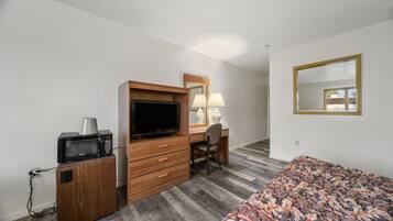 Habitación de hotel con escritorio de madera, televisor, microondas, una silla, cama con colcha estampada y un espejo grande en la pared.