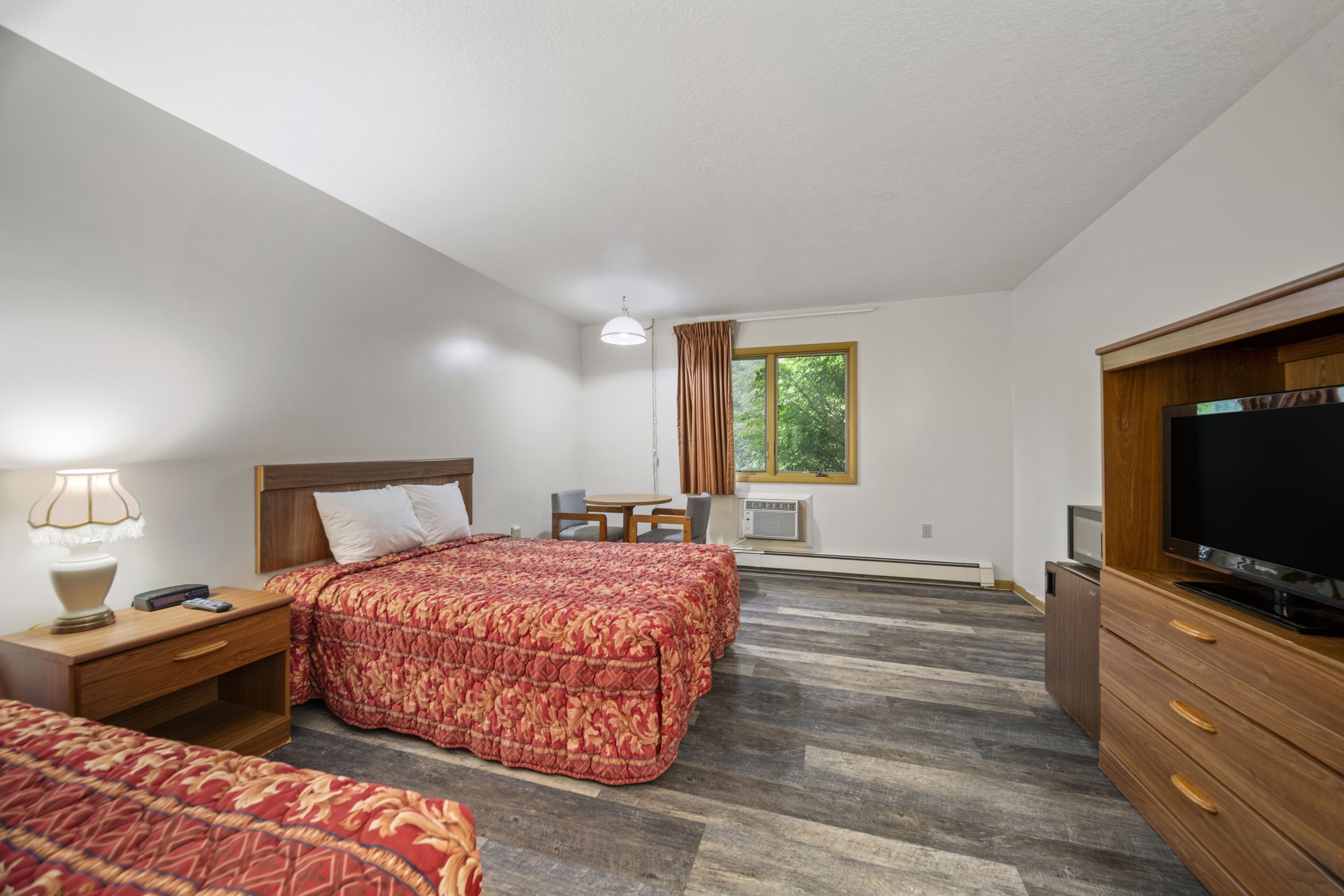 Une chambre d’hôtel avec deux lits, une télévision, un bureau et une fenêtre avec des rideaux.