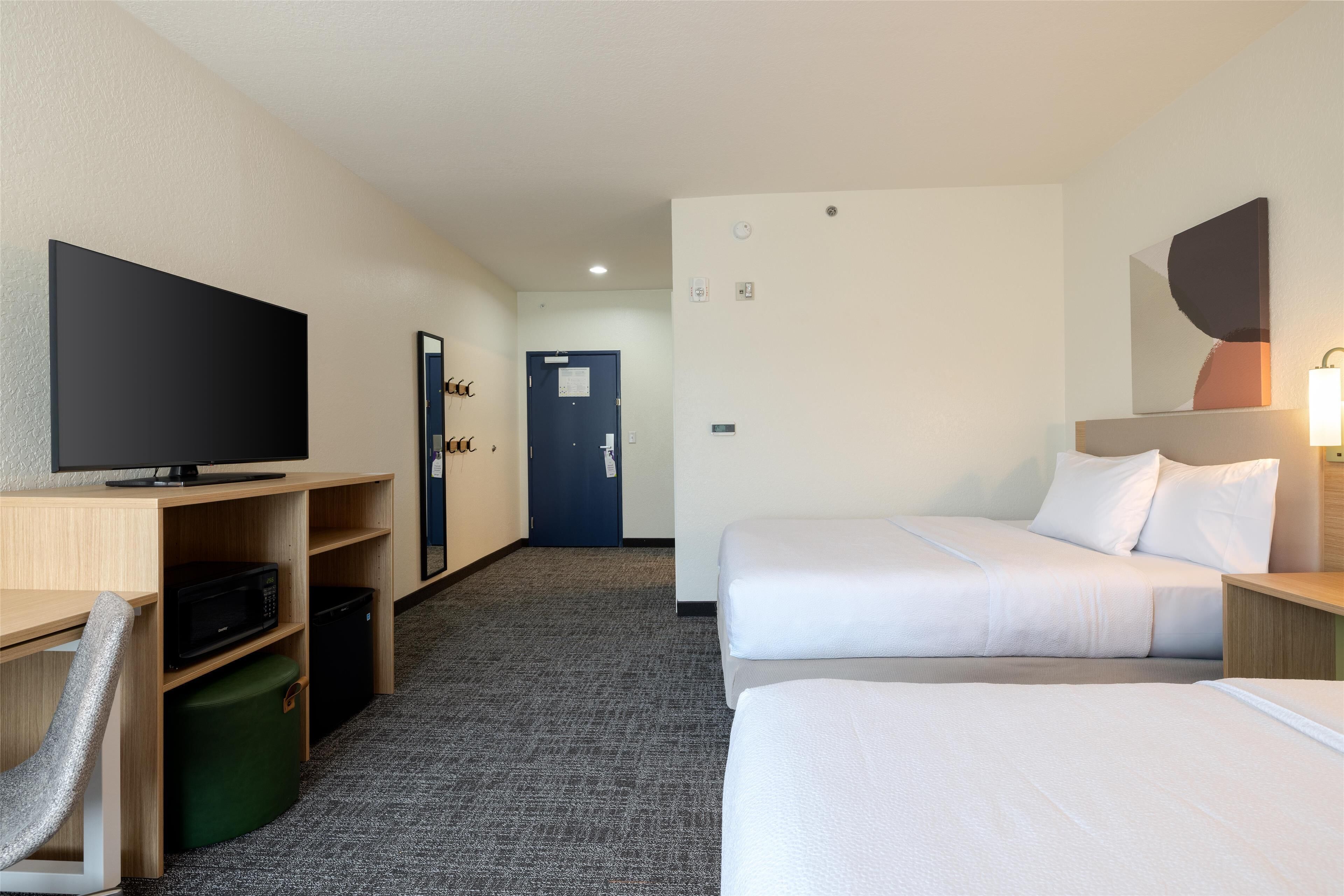 A hotel room with two beds, a desk with a television, a microwave, and a trash bin.