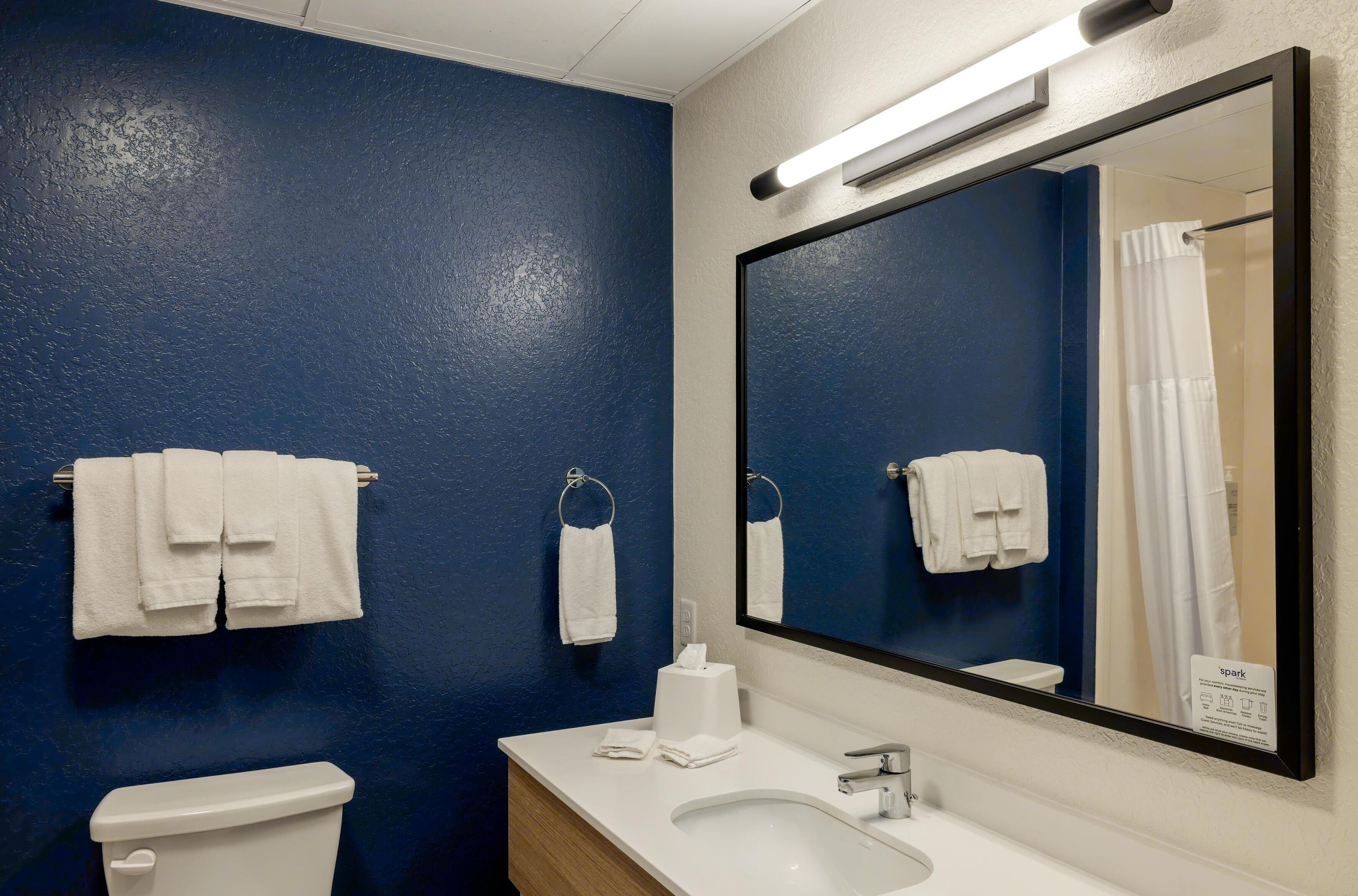 Baño con pared azul, accesorios blancos y un espejo grande.