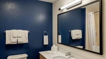 A bathroom with a blue wall, white fixtures, and a large mirror.