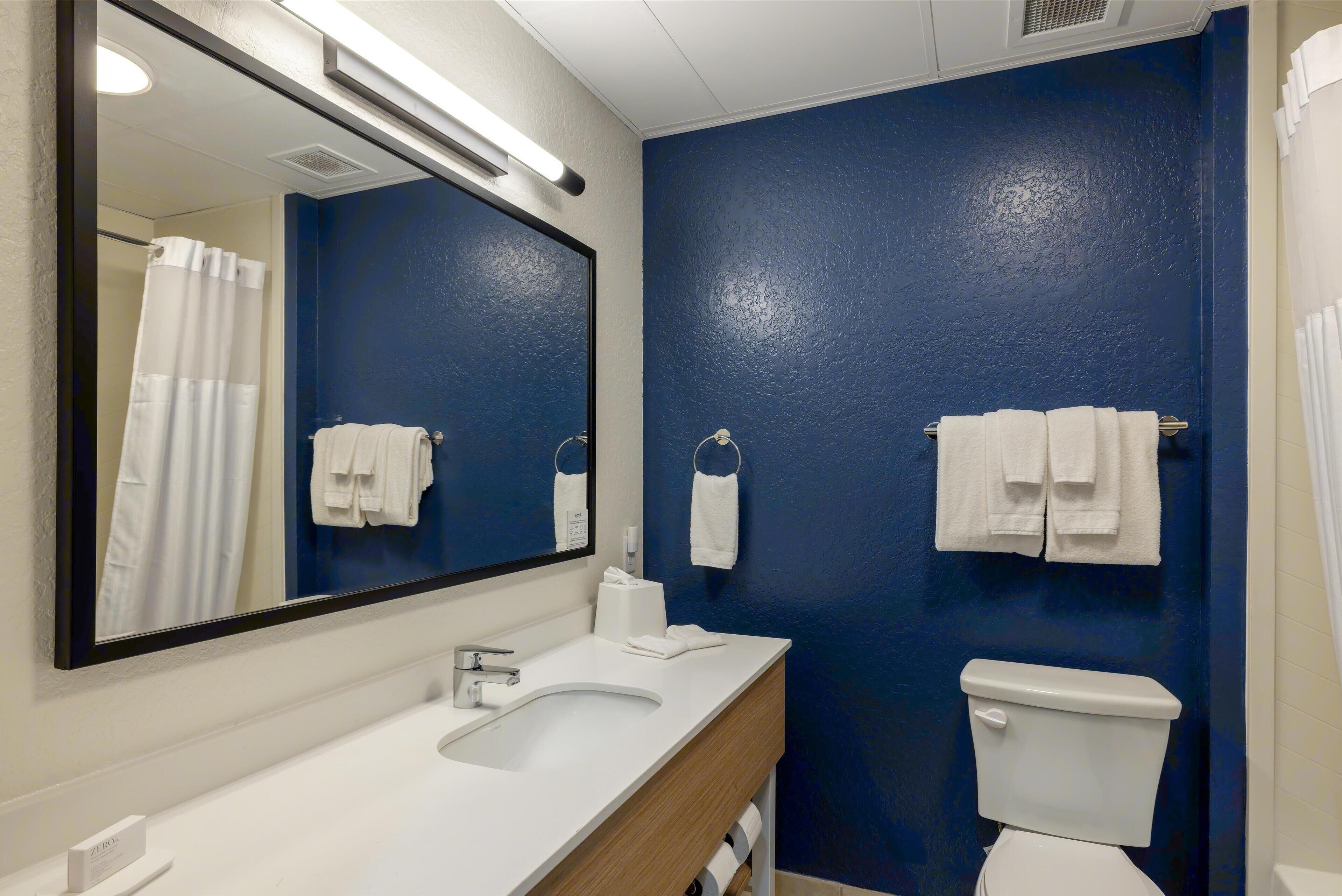 A bathroom with a white sink, a mirror, a toilet, and towels hanging on the wall.