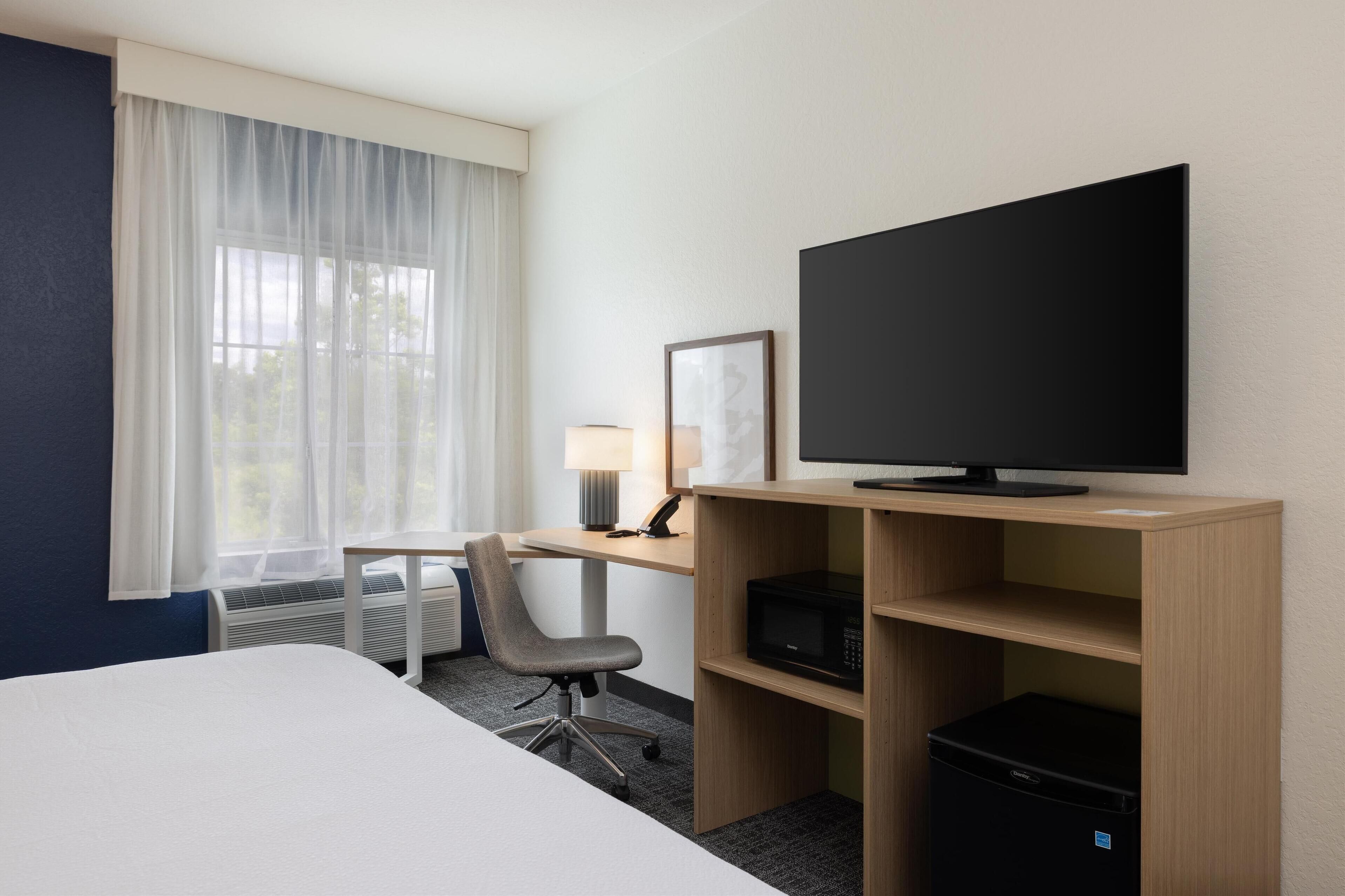 A hotel room with a bed, a desk with a computer, a television, and a chair.