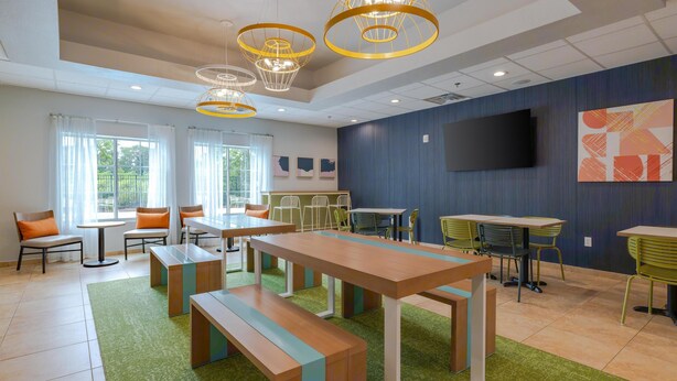 Un hall moderno de hotel con alfombra verde, bancos de madera y un televisor grande en la pared.
