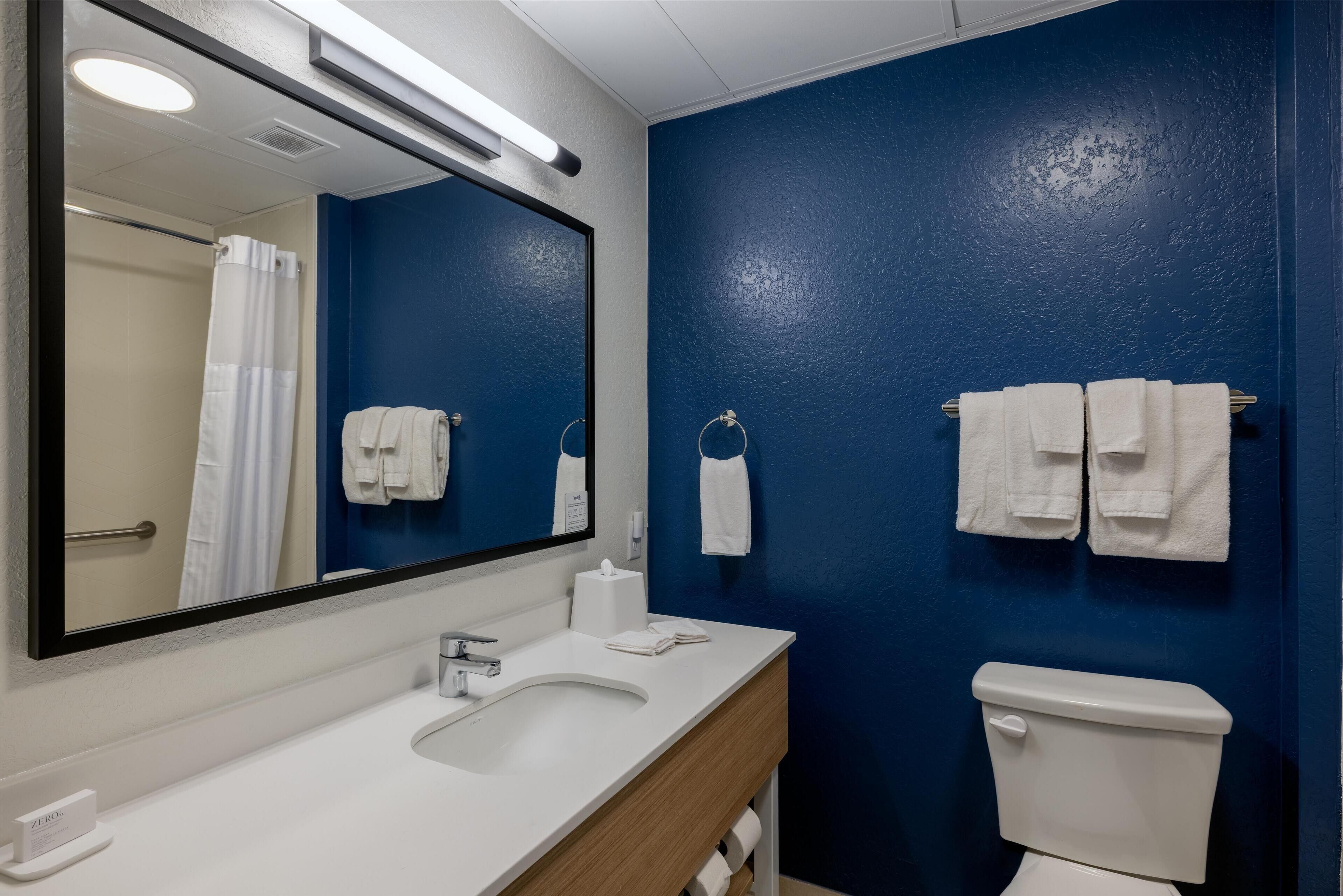 Un baño con un lavamanos blanco, un espejo, un inodoro y toallas colgadas en la pared.