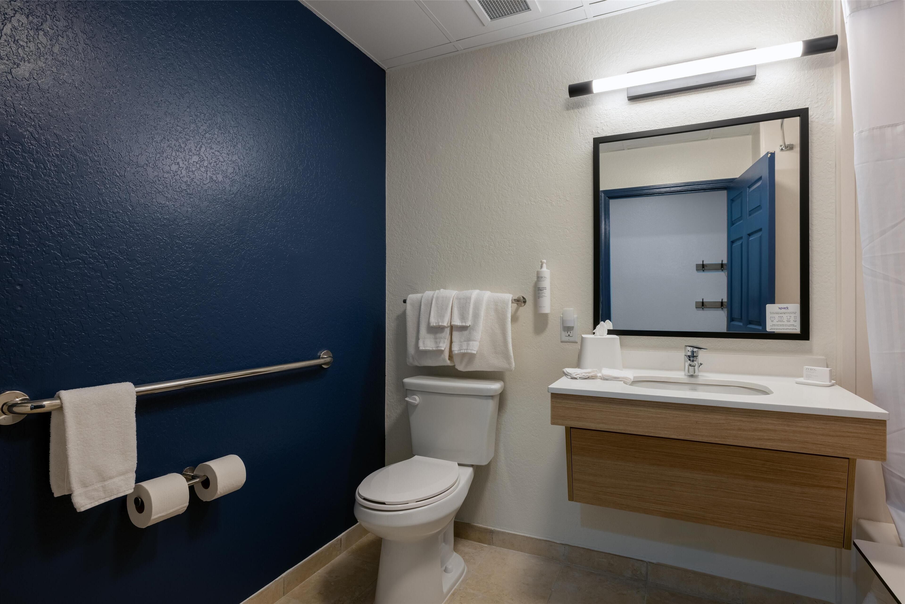 A bathroom with a blue wall, a white toilet, a sink with a mirror, and a towel rack.