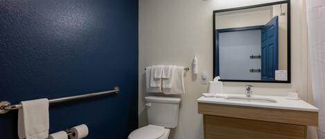 A bathroom with a blue wall, a white toilet, a sink with a mirror, and a towel rack.