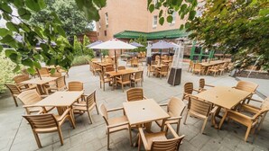Un patio exterior con varias mesas y sillas de madera, rodeado por un edificio de ladrillo.