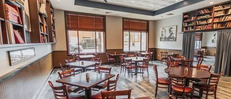 A restaurant with multiple tables and chairs, large windows, ceiling fans, and bookshelves.