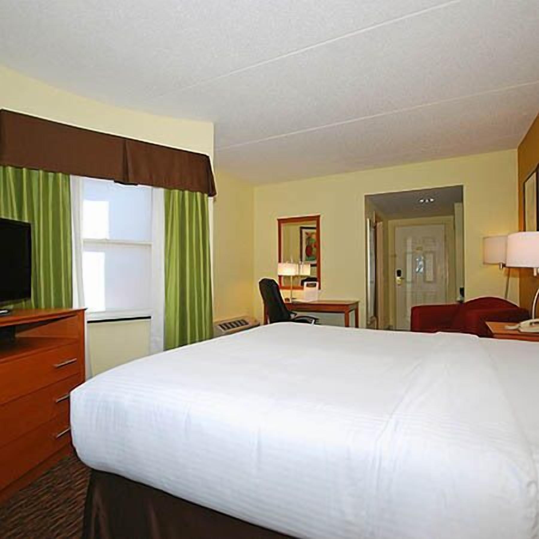 A hotel room with a large bed, a desk, a chair, a television, and a door.