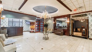 Un vestíbulo de hotel con mostrador de recepción, zona de estar, candelabro y un letrero que dice 'University Grille'.