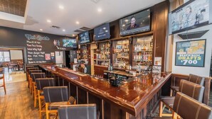 Zona de bar con una barra larga, diversas opciones de asientos y una pantalla de televisión mostrando un programa.
