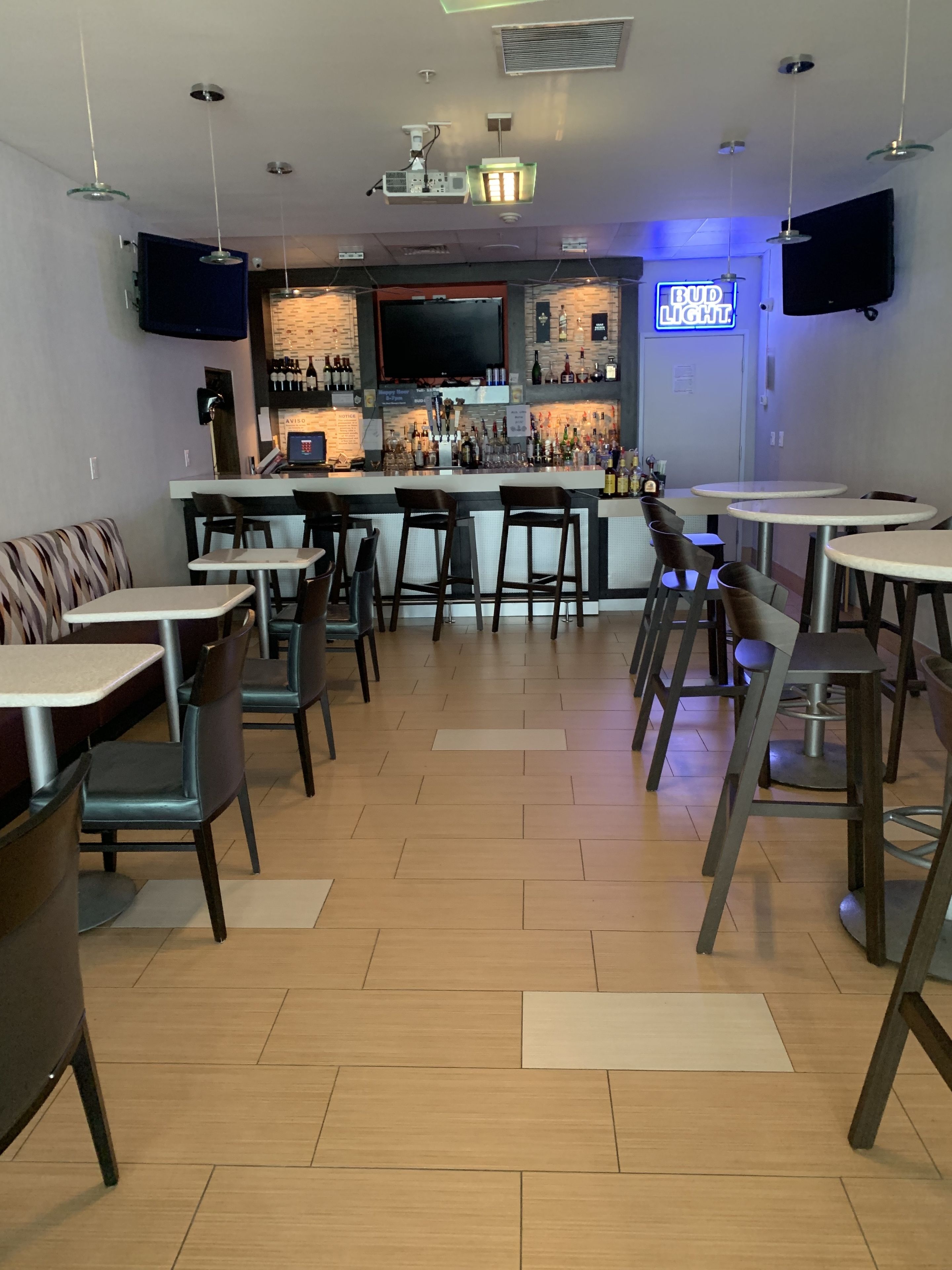A bar area with a counter, bar stools, and a neon sign.