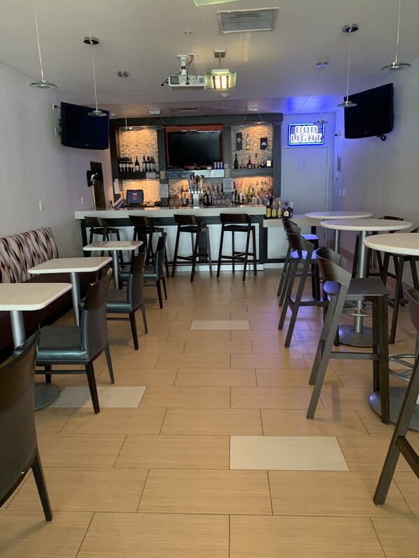 A bar area with a counter, bar stools, and a neon sign.