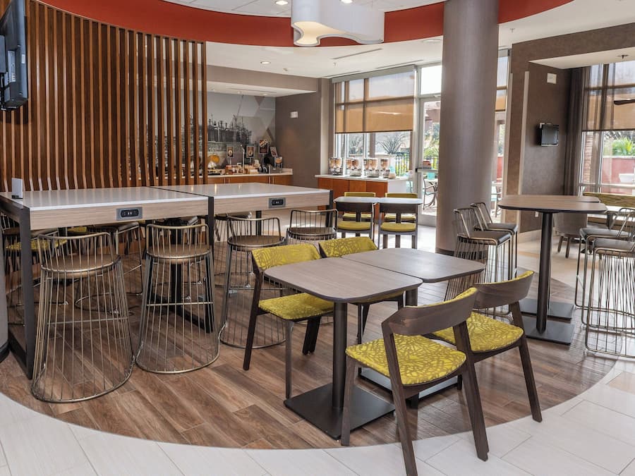 A modern restaurant with a bar area, multiple seating options including tables and chairs, and large windows providing natural light.